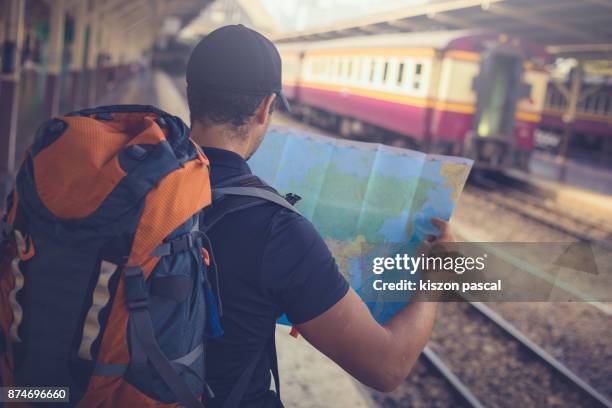 young man backpacker looking at the map while waiting for a train in railway station . - open roads world premiere of mothers day arrivals stockfoto's en -beelden