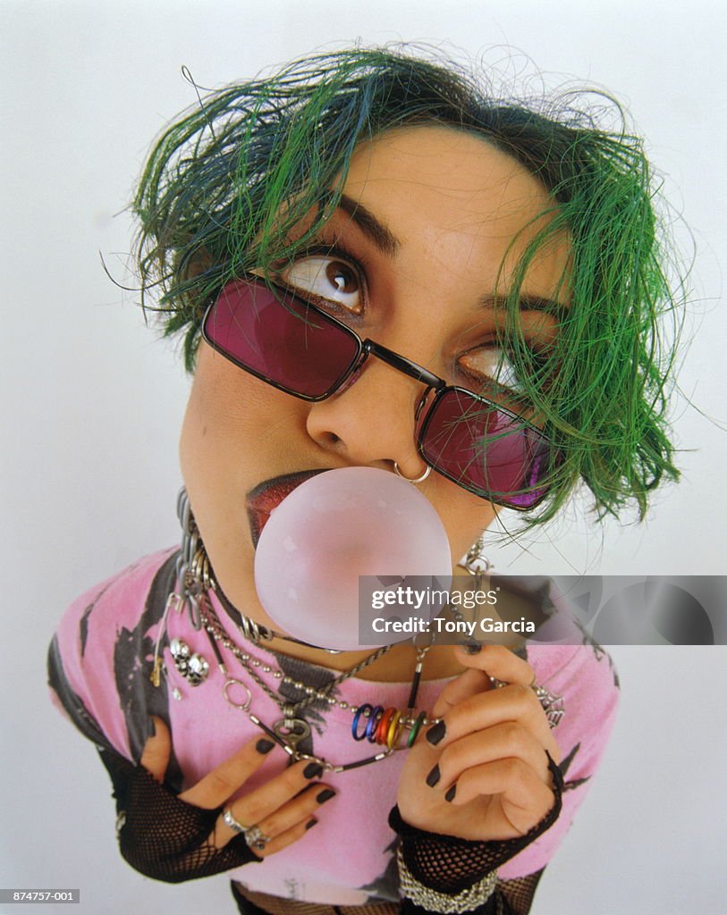 Teenage girl (16-18) blowing bubble gum bubble, portrait (wide angle)