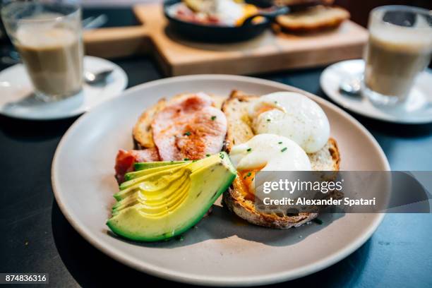 breakfast with poached eggs, avocado, bacon and toasted bread - roggebrood stockfoto's en -beelden