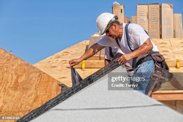 roofer tears off protective cover of underlayment on a new roof - membrana imagens e fotografias de stock