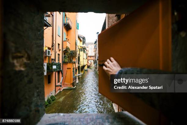 man opening window and looking at the canal in bologna, italy - durch loch schauen stock-fotos und bilder