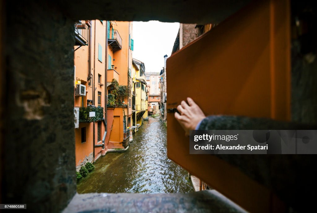 Man opening window and looking at the canal in Bologna, Italy