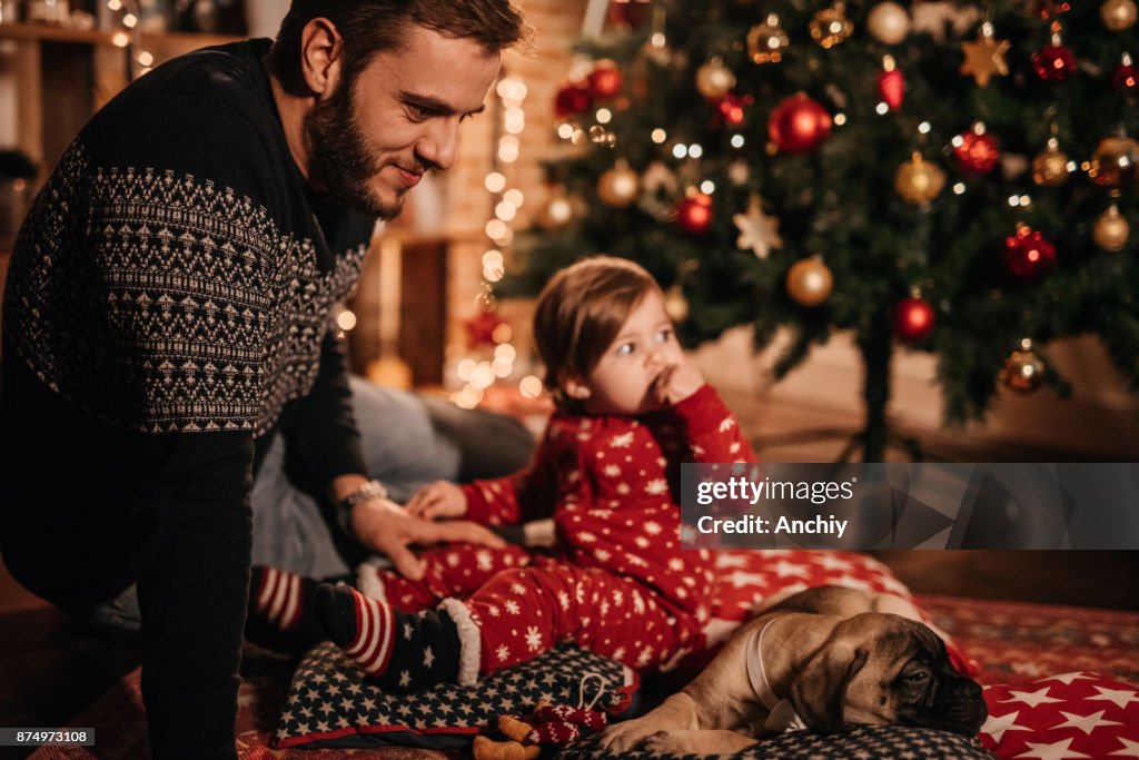 Dad and daughter sitting by the Christmas tree with their puppy