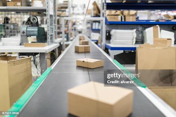 cardboard boxes on conveyor belt at distribution warehouse - embrulhar imagens e fotografias de stock
