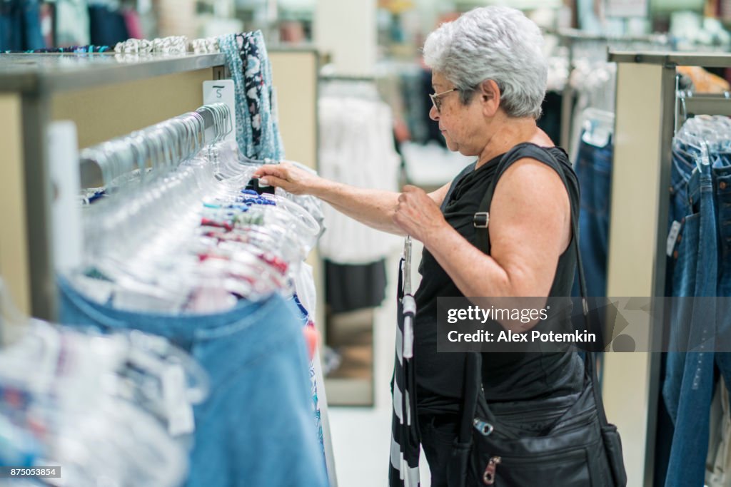 The silver-haired 65-years-old active senior woman shopping in the clothing retail store