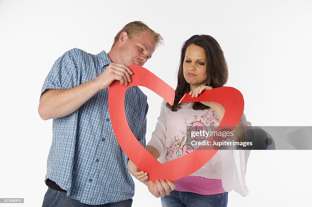 Couple holding two torn parts of a heart