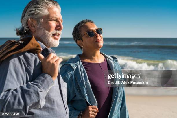 the senior couple, african-american woman and silver haired, bearded white man, walking at the jones beach - alex potemkin or krakozawr latino fitness stock pictures, royalty-free photos & images