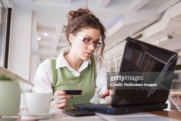 single. curly, red hair young woman, drinking coffee, making a online credit card purchase on laptop in local cafe - curly red hair glasses stock pictures, royalty-free photos & images