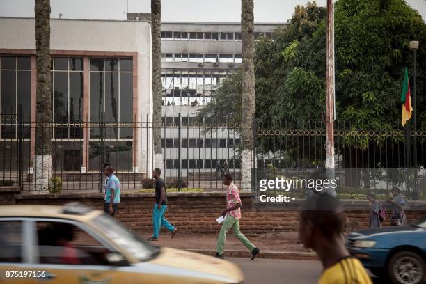 People walk by the damaged building of Cameroon's parliament on November 17, 2017 in Yaounde, after a fire swept through the main building overnight,...