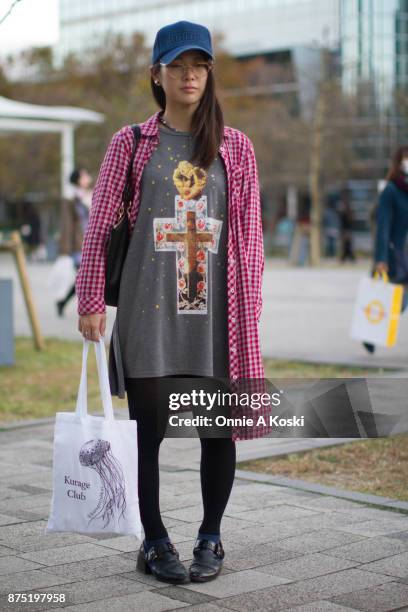 Aki stops for a quick fashion snap wearing a grey Jóueie t-shirt featuring a gold cupid on a cross suspended in resin with roses on a starry...