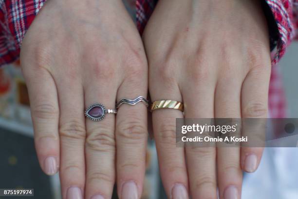 Close of Aki's silver and gold rings. Aki stops for a quick fashion snap wearing a grey Jóueie t-shirt featuring a gold cupid on a cross suspended in...