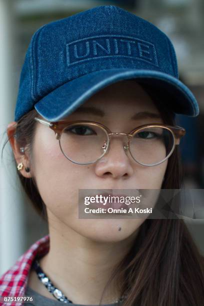 Portrait of Aki wearing half framed horn rimmed brown glasses and a denim blue baseball cap by Unite. Aki stops for a quick fashion snap wearing a...