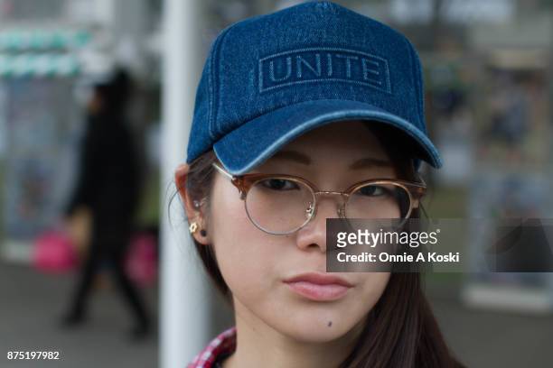 Portrait of Aki wearing half framed horn rimmed brown glasses and a denim blue baseball cap by Unite. Aki stops for a quick fashion snap wearing a...