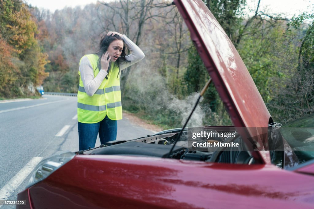 Young stressed woman looking at her broken down car
