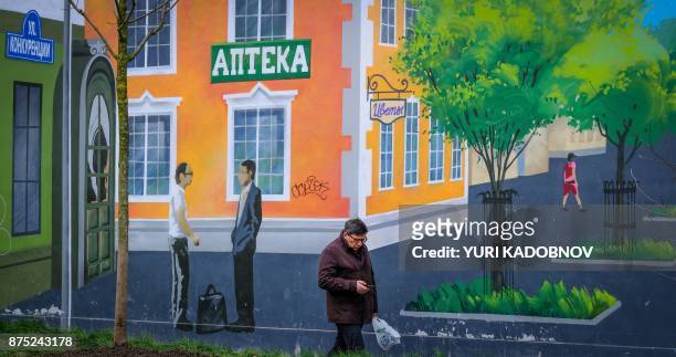 Man uses a mobile phone while walking past a city themed mural on the wall of a building in Moscow on November 17, 2017. / AFP PHOTO / Yuri KADOBNOV