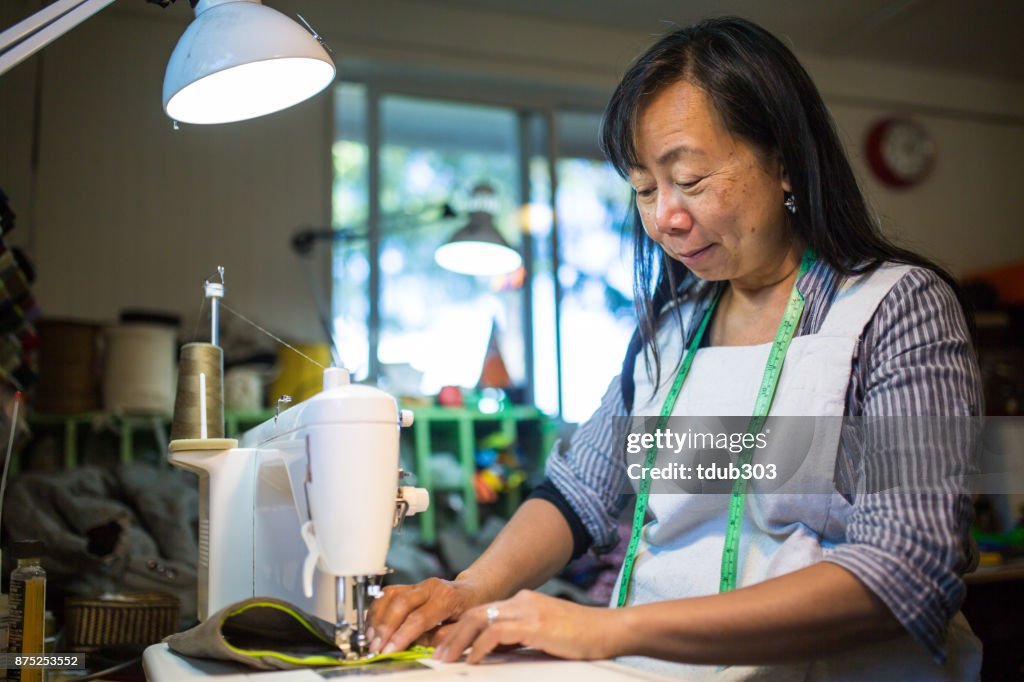 Een volwassen vrouw die werkt met een naaimachine in een kleine kunststudio