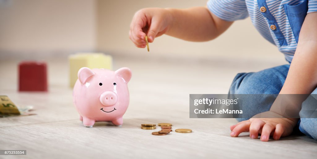 Two years old child sitting on the floor and putting a coin into a piggybank