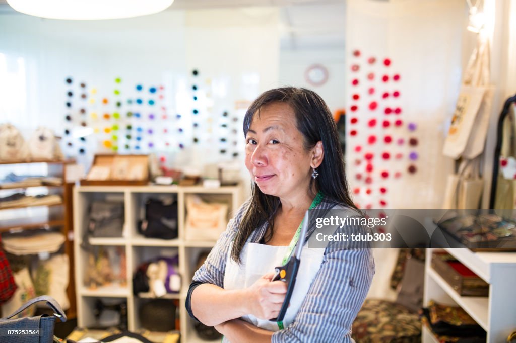 Een volwassen ondernemer in haar shop van upcycled handgemaakte tassen houden een digitale tablet