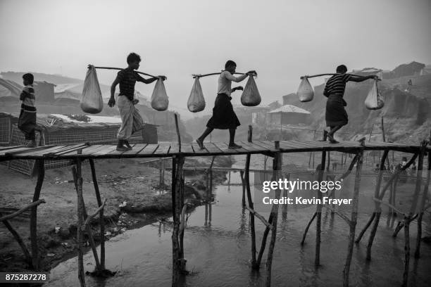 Rohingya Muslim refugee men carry food aid across makeshift bamboo bridges on October 27, 2017 at the Kutupalong refugee camp in Cox's Bazar,...