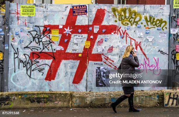 Woman speaks on a mobile phone as she walks past a graffiti covered wall with a giant hashtag sign near Moscow's Kursky railway station on November...