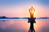 Silhouette young woman practicing yoga lotus position, meditating, beach