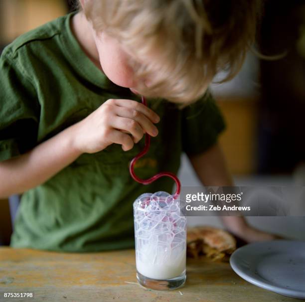 young caucasian boy blowing milk bubbles - straw ストックフォトと画像