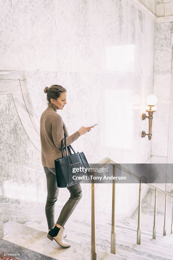 Young business woman checking phone on stairs in public building