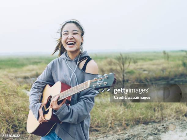 fashionable woman playing guitar on country road - chinese music imagens e fotografias de stock