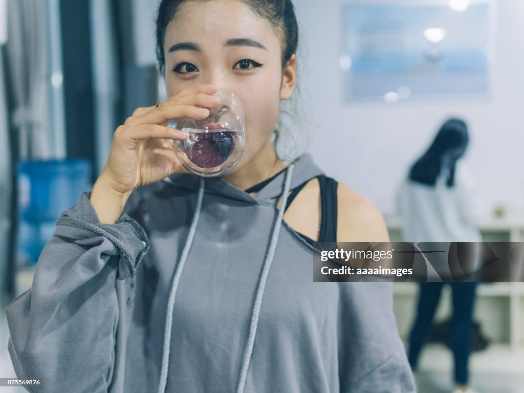 Female dancer drinking a glass of water after dancing in studio