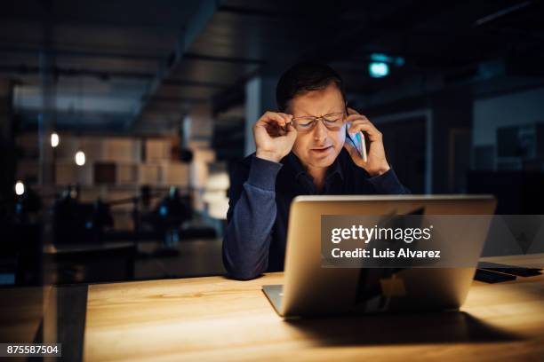 frustrated businessman using phone while working late on laptop - workaholic stock-fotos und bilder