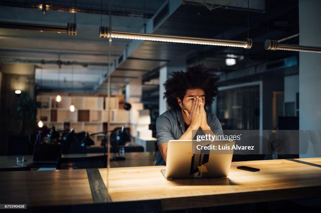 Tired businessman working on laptop at desk