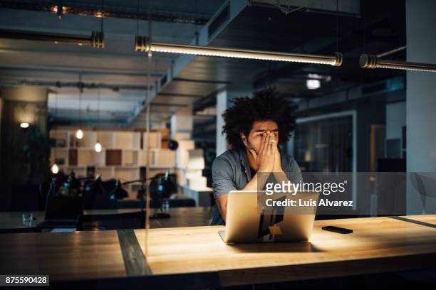 tired businessman working on laptop at desk - frustrazione foto e immagini stock
