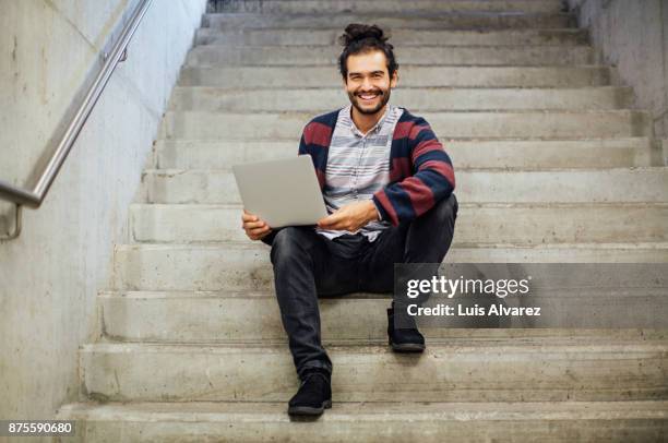 portrait of businessman holding laptop while sitting on steps - man bun stock pictures, royalty-free photos & images