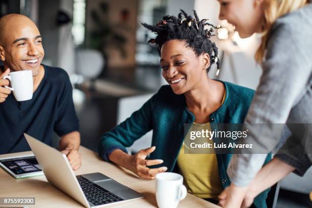 happy business colleagues talking while using laptop at office - drei erwachsene stock-fotos und bilder