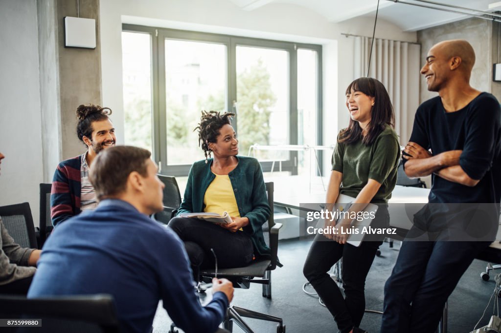 Colleagues looking at cheerful businesswoman in meeting