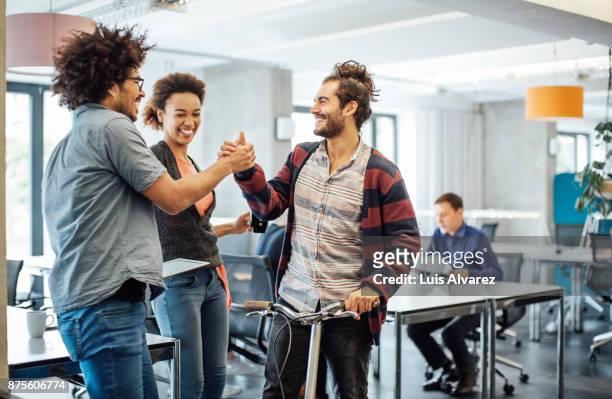 happy colleagues greeting to businessman with push scooter - career vitality stock pictures, royalty-free photos & images