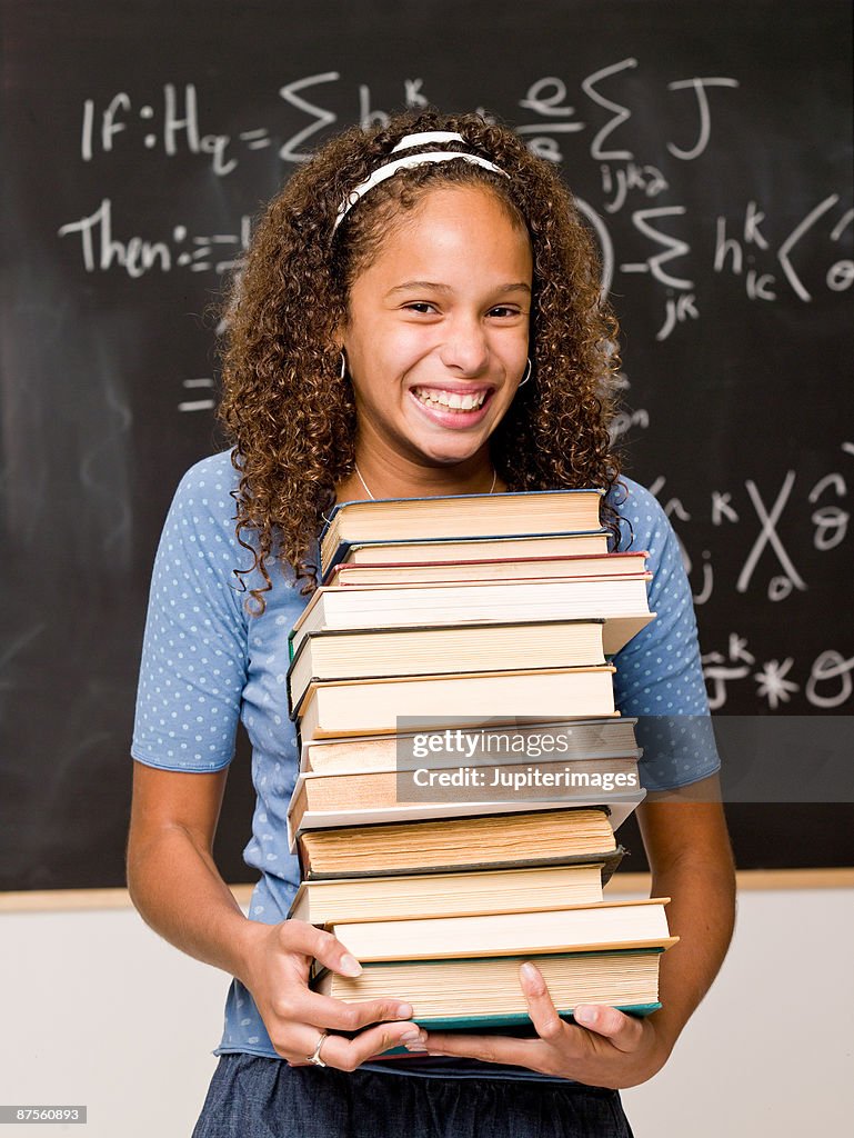 Teenage girl student posing in classroom with stack of books