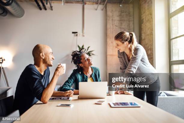 business colleagues talking while using laptop at office - three people office stock pictures, royalty-free photos & images