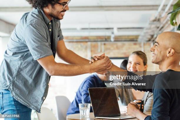 smiling businessmen holding hands by colleagues at table - hi 5 stock pictures, royalty-free photos & images