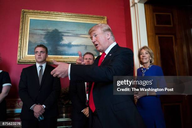 President Donald Trump, with Education Secretary Betsy DeVos by his side, gestures as he walks in to greet the West Virginia University rifle team...