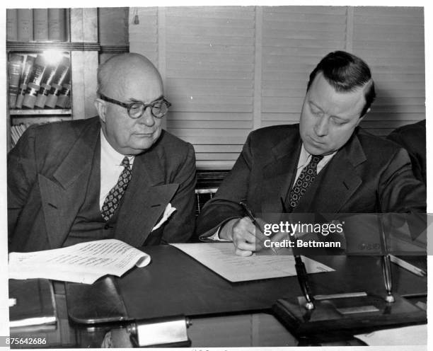 While Henry J. Kaiser, Chairman of the Board of Kaiser-Frazer Corporation looks on, Walter P. Reuther, President of the UAW, CIO, signs an agreement...