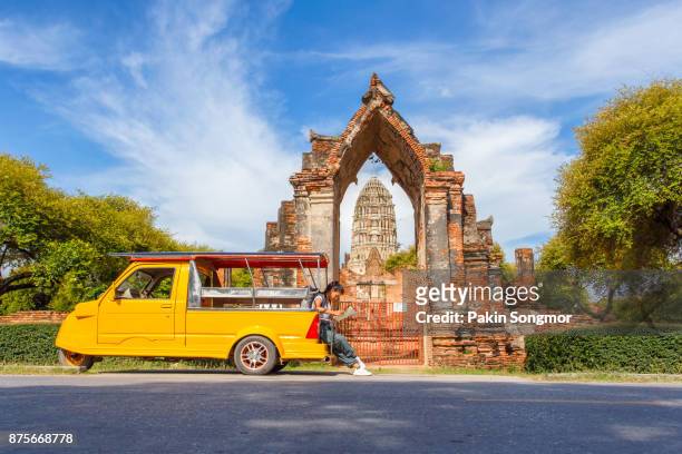 young asian female traveler with backpack traveling sitting on taxi or tuk tuk and see map travel with old temple (wat mahathat) background, ayutthaya province, thailand - チェンマイ県 ストックフォトと画像