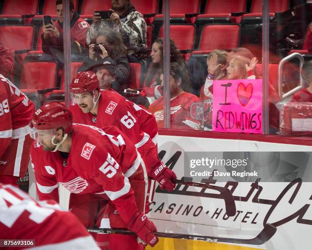 Young fan holds up a sign behind Xavier Ouellet of the Detroit Red Wings prior to an NHL game against the Calgary Flames at Little Caesars Arena on...