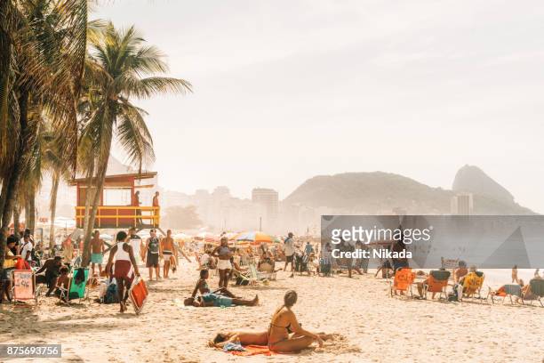 people relaxing and sunbathing at famous copacabana beach, rio de janeiro, brazil - rio de janeiro stock pictures, royalty-free photos & images