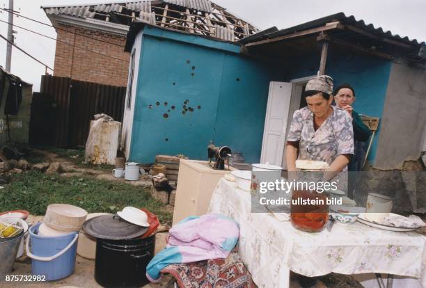 Eine Bäuerin beim Backen vor ihrem zerstörten Haus in Tschetschenien. Möbel und Haushaltsgegenstände stehen vor dem Gebäude. Eine der Hauswände ist...
