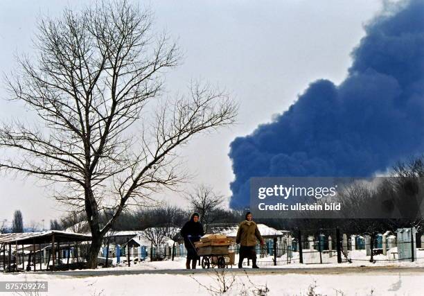 Bewohner von Grosny nutzen einen Handkarren zum Transport, im Hintergrund die brennende Ölraffinerie von Grozny Januar 1995