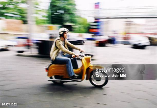 Mann fährt auf einem orange-gelbem Motorroller