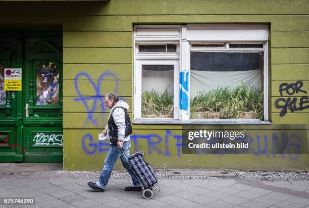 Deutschland Germany Berlin Passant läuft mit seinem Einkaufswagen an einem Graffiti ' Gentrifizierung' in der Neuöllner Weserstrasse vorbei.