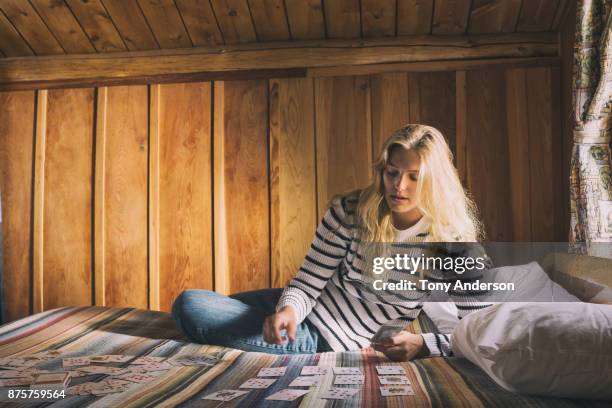 young woman playing cards on bed in rustic cabin - id card stockfoto's en -beelden