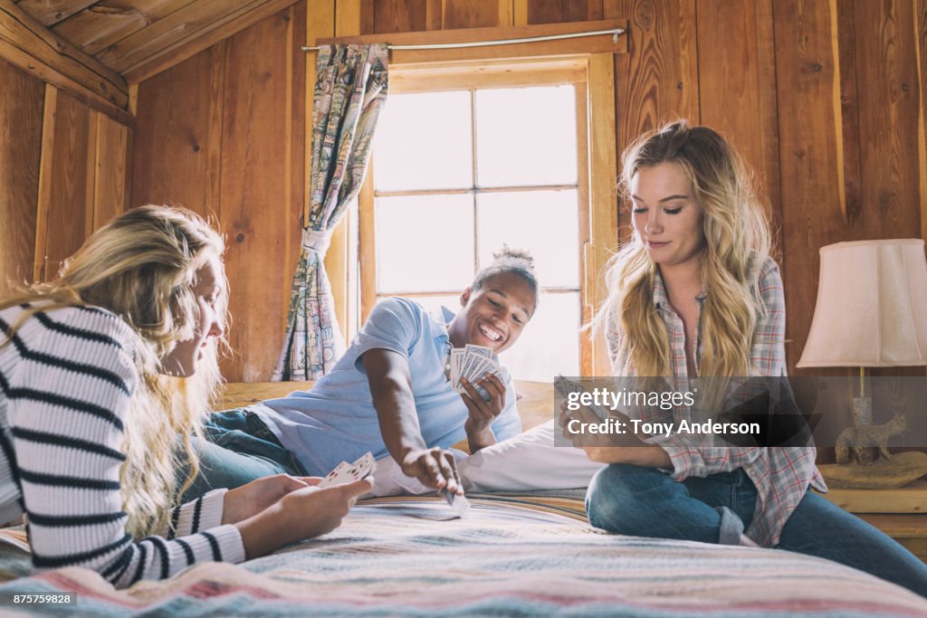 Teenage friends playing cards on bed in rustic cabin